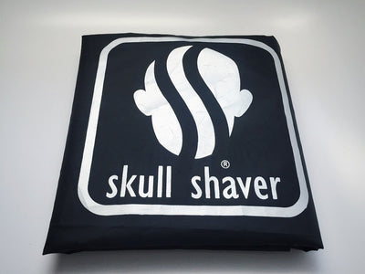 Barber's Hair Cutting Cape folded with  skull shaver logo in it.